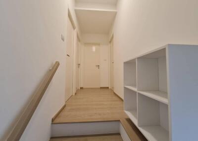 A minimalistic hallway with wooden flooring, white walls, and an open shelf unit.