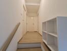 A minimalistic hallway with wooden flooring, white walls, and an open shelf unit.