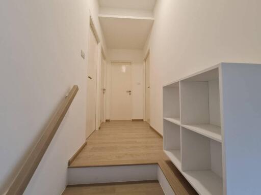 A minimalistic hallway with wooden flooring, white walls, and an open shelf unit.