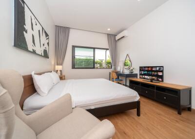 Modern bedroom with a double bed, large window, desk, chair, TV, and air conditioning unit