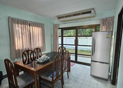 Dining area with a glass-top wooden table and four chairs, air conditioning unit, refrigerator, and large windows with curtains