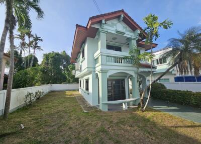 Exterior view of a two-story house with a lawn and palm trees