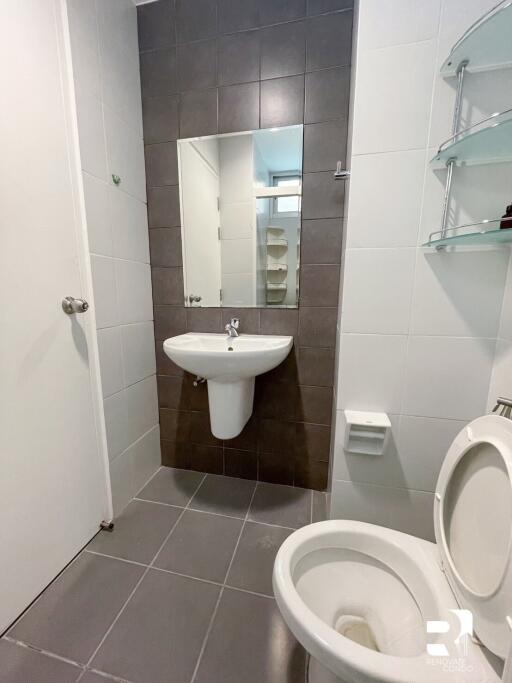 Modern bathroom with tiled walls and floor, featuring a wall-mounted sink and toilet