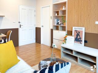 Modern living room with wooden floor, white door, shelving, and art decorations