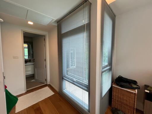 Hallway with wooden flooring, window blinds, and view into bathroom