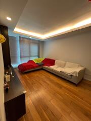 Living room with wooden floor, L-shaped couch, and large windows with blinds