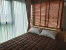 A cozy bedroom with large window and brown blinds