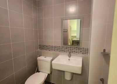 Modern bathroom with grey tiles, a white toilet, and a wall-mounted sink with a mirror