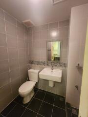 Modern bathroom with grey tiles, a white toilet, and a wall-mounted sink with a mirror