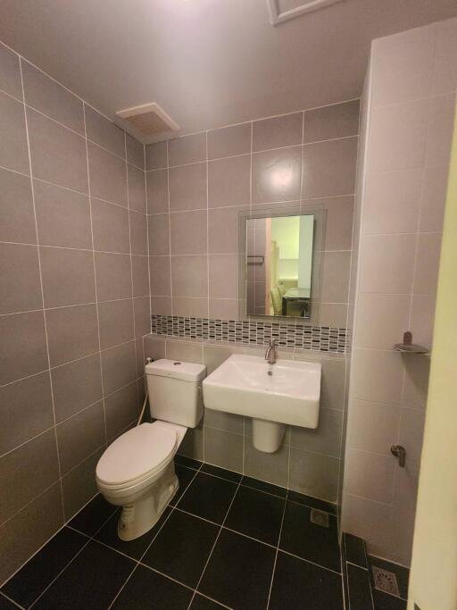 Modern bathroom with grey tiles, a white toilet, and a wall-mounted sink with a mirror