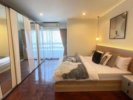 Spacious and well-lit bedroom with a large bed, mirrored wardrobes, wooden flooring, and modern decor.