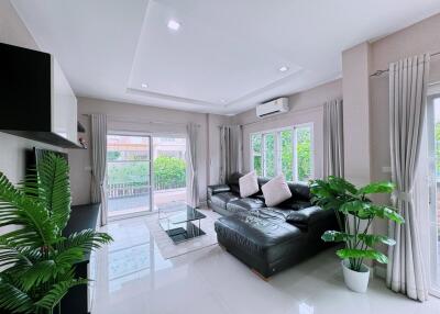 Modern living room with large black leather sofa, glass coffee table, wall-mounted television, and large windows with curtains