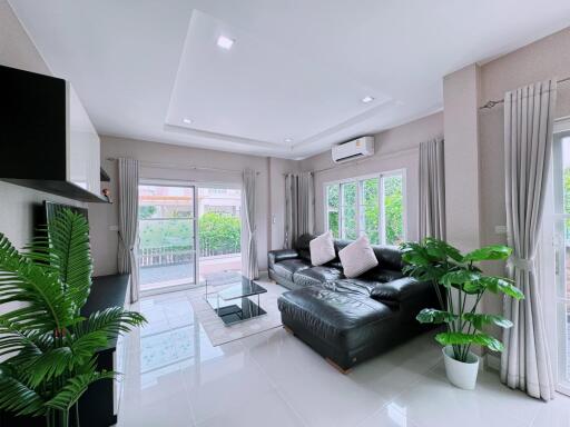 Modern living room with large black leather sofa, glass coffee table, wall-mounted television, and large windows with curtains