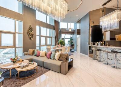 Modern and spacious living area with high ceilings, chandelier lighting, and large windows