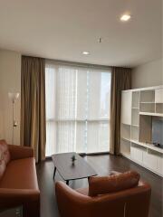 Modern living room with large windows, brown sofas, floor lamp, coffee table, and built-in shelving unit