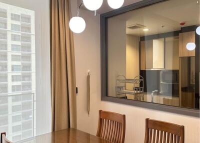 Modern dining room with a large window, wooden furniture, and a view into the adjacent kitchen