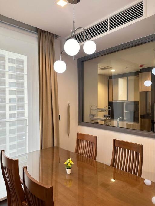 Modern dining room with a large window, wooden furniture, and a view into the adjacent kitchen