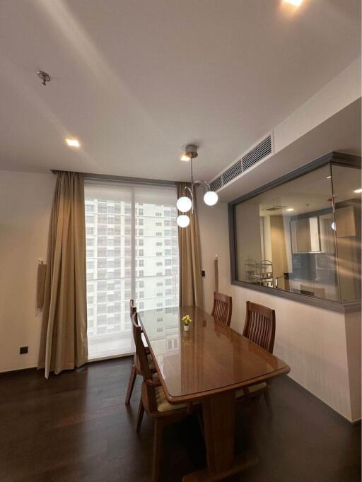 Modern dining room with wooden table and chairs, large window with curtains, and hanging lights