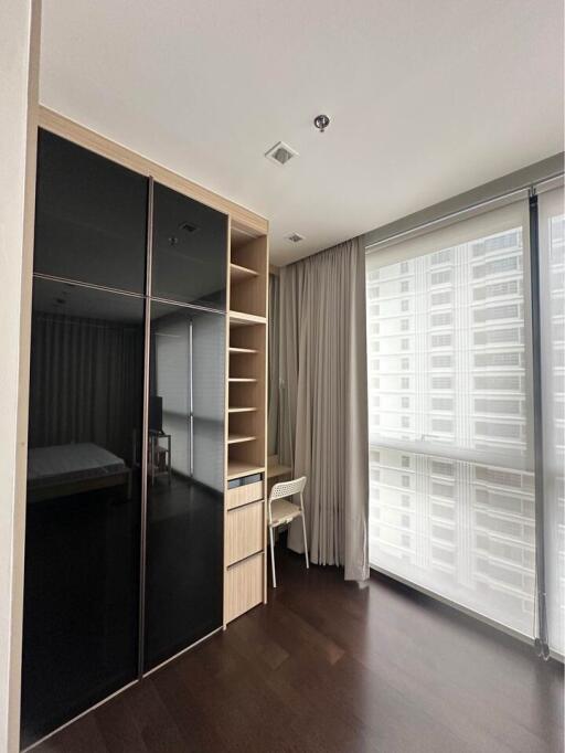 Modern minimalist bedroom with large window, dark flooring, black and wood wardrobe, and small desk by the window