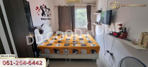 Bedroom with a large bed and colorful bedding, wall decorations, a mounted TV, and window with curtains