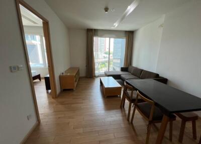 Modern living room with wooden flooring, a large window, sofa, dining table, and chairs