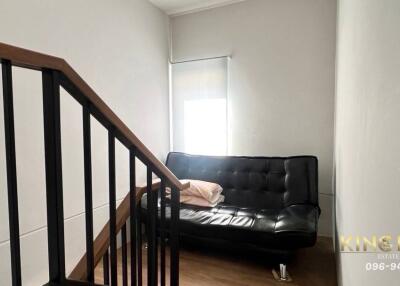 Small living room with a black leather sofa and a wooden staircase