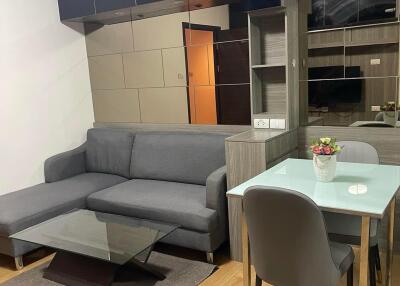 Modern living and dining area with gray sofa, glass coffee table, and a small dining table with chairs