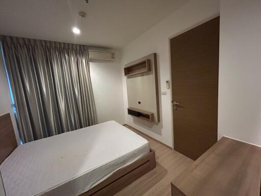 modern bedroom with a bed, window with curtains, wall-mounted air conditioner, wooden door, and dresser