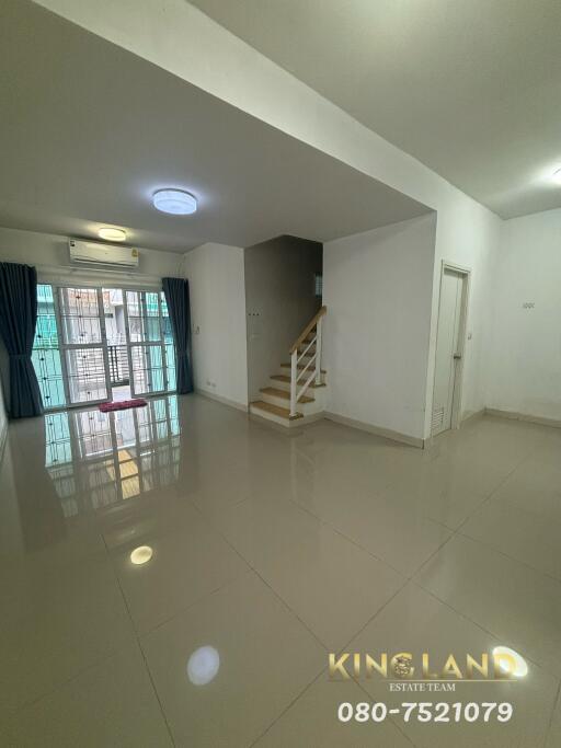 Spacious living room with glossy tile flooring, staircase, and large window with curtains