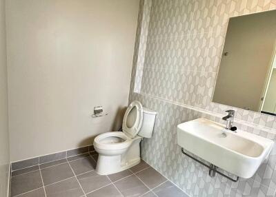 A modern bathroom with tiled walls and flooring, featuring a toilet and a wall-mounted sink with a mirror.