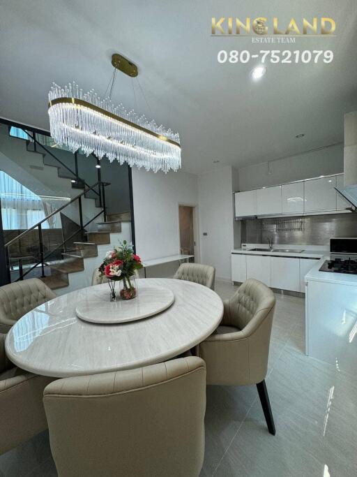 Modern dining area with kitchen, chandelier, and staircase