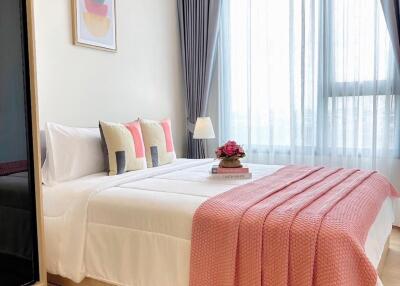 Cozy bedroom with a double bed, pink throw blanket, decorative pillows, artwork, and large window with curtains