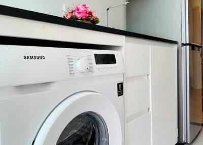 A kitchen area with white cabinets, a washing machine, and a refrigerator.