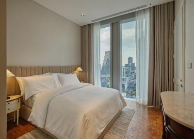 A bedroom with a large bed, bedside tables with lamps, large windows with a city view, and a dressing table.