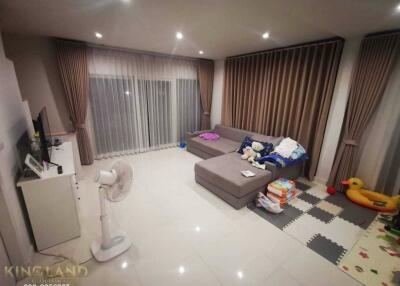 A cozy living room with a sectional sofa, toys on the floor, a fan, and a TV stand.