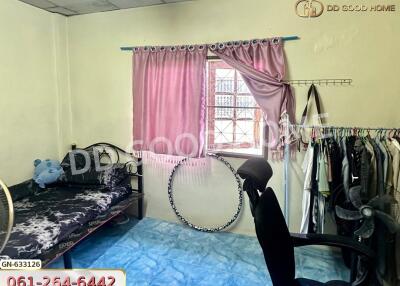 A cozy bedroom with a single bed, window with pink curtains, office chair, and clothing rack