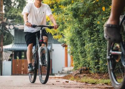 Two cyclists riding on a paved path with trees and houses in the background