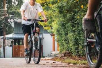 Two cyclists riding on a paved path with trees and houses in the background