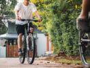 Two cyclists riding on a paved path with trees and houses in the background