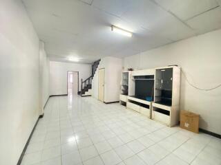 A spacious living room with white tiled floor, a large entertainment unit, and a staircase leading to the upper level.