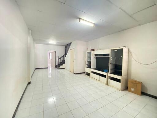 A spacious living room with white tiled floor, a large entertainment unit, and a staircase leading to the upper level.