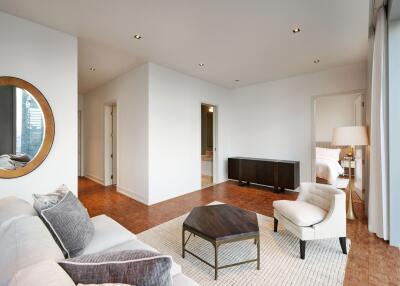 Modern living room with white walls, a beige sofa, a wooden coffee table, contemporary decor, and an adjoining bedroom.