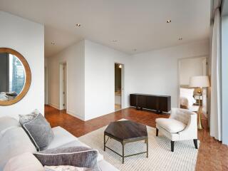 Modern living room with white walls, a beige sofa, a wooden coffee table, contemporary decor, and an adjoining bedroom.