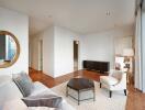 Modern living room with white walls, a beige sofa, a wooden coffee table, contemporary decor, and an adjoining bedroom.