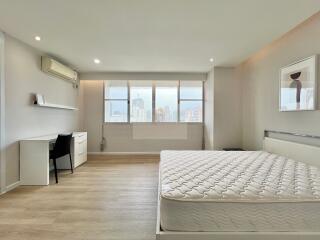 Spacious, modern bedroom with a large window, desk, and bed.