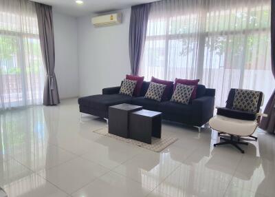 Contemporary living room with large windows, black sofa, and white tile flooring