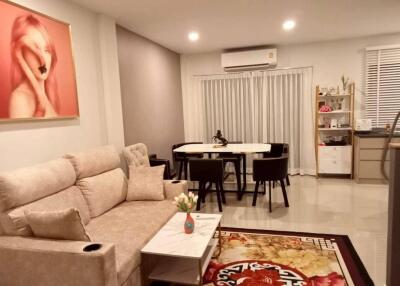 Modern living room featuring a comfortable sofa, wall art, a dining area with six chairs, an air conditioning unit, and decorative accents.