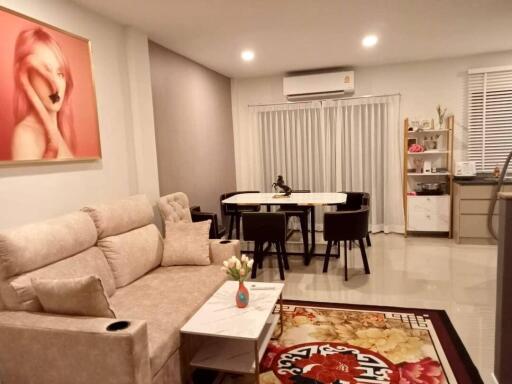 Modern living room featuring a comfortable sofa, wall art, a dining area with six chairs, an air conditioning unit, and decorative accents.