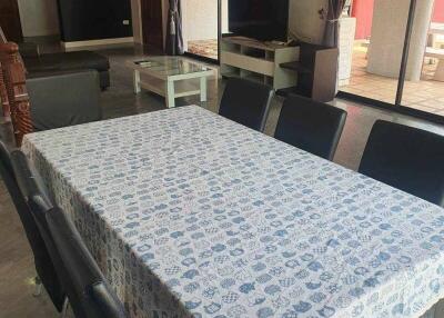 Dining room with a long table and chairs, adjacent to the living area with a TV and access to a balcony