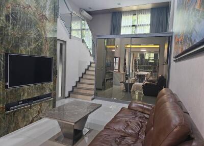 Modern living room with staircase, TV, and leather sofa